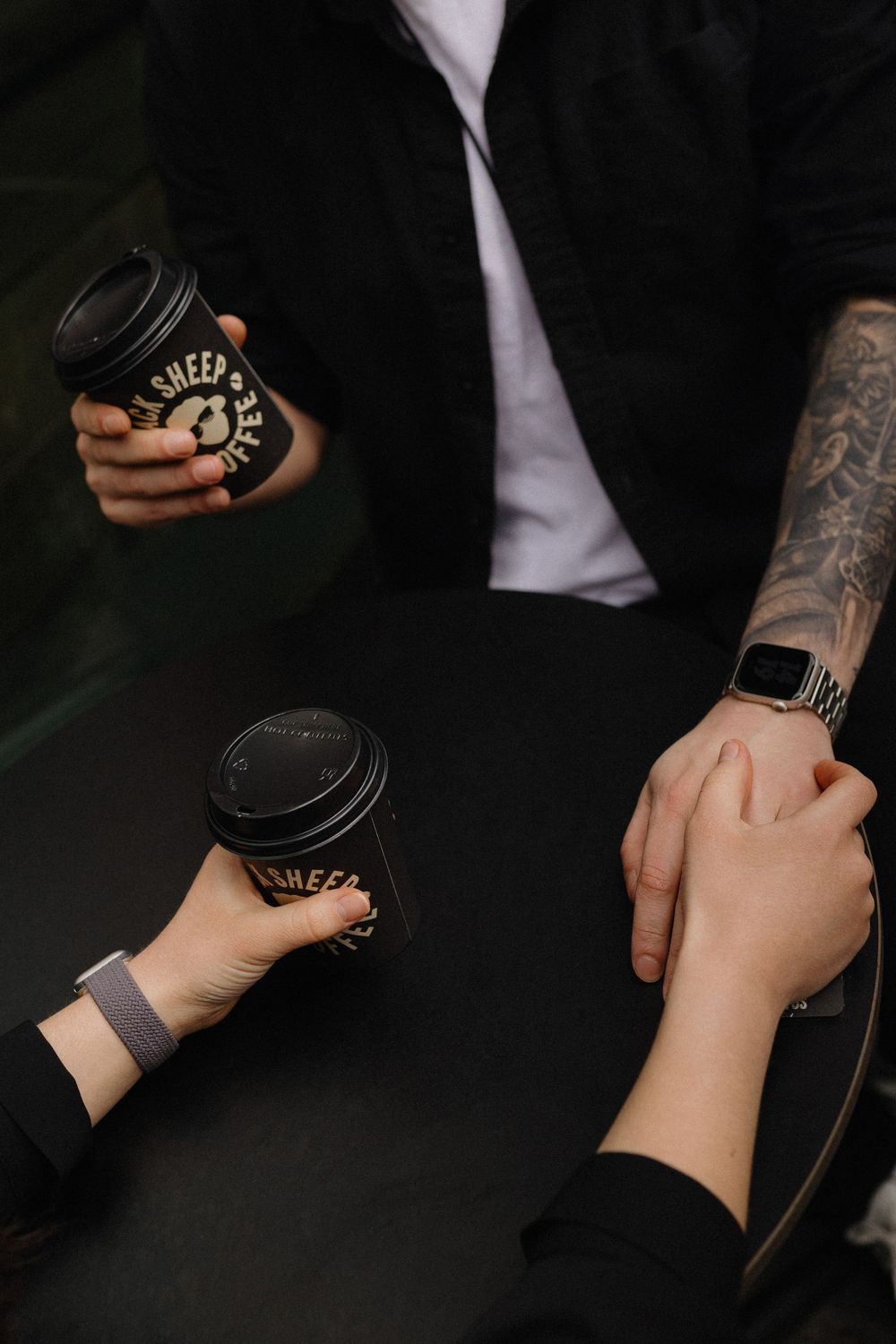 Close-up shots of hands holding black coffee cups against a dark background with tattoo details visible.