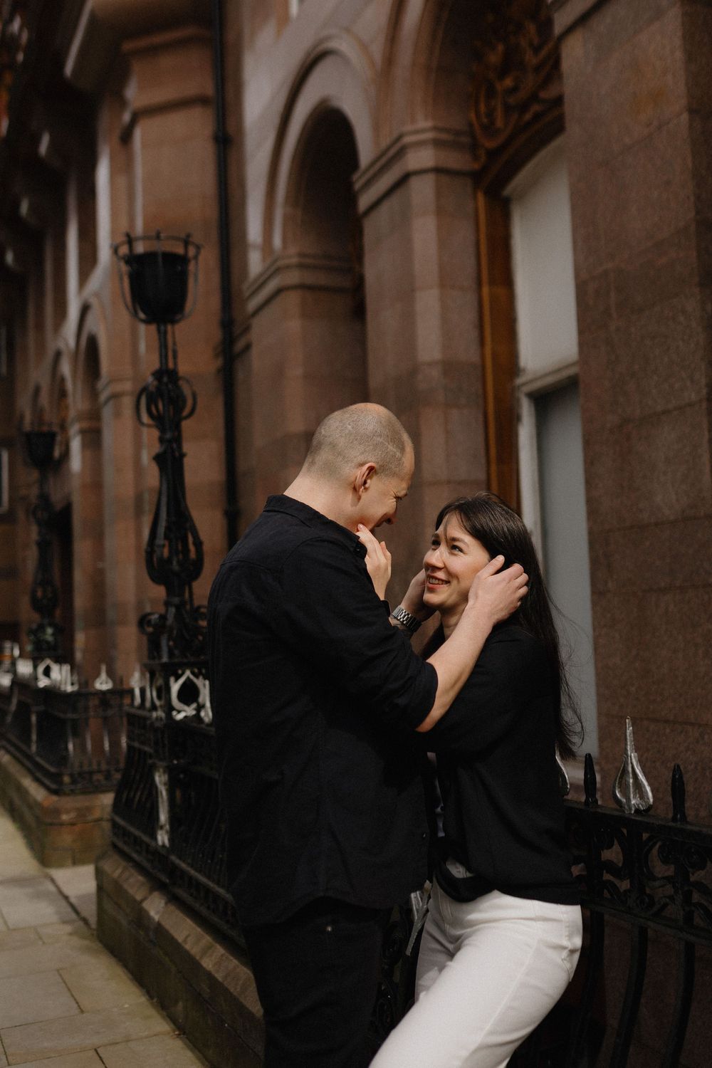 A romantic couple shares intimate moments under an ornate stone archway with vintage lanterns.