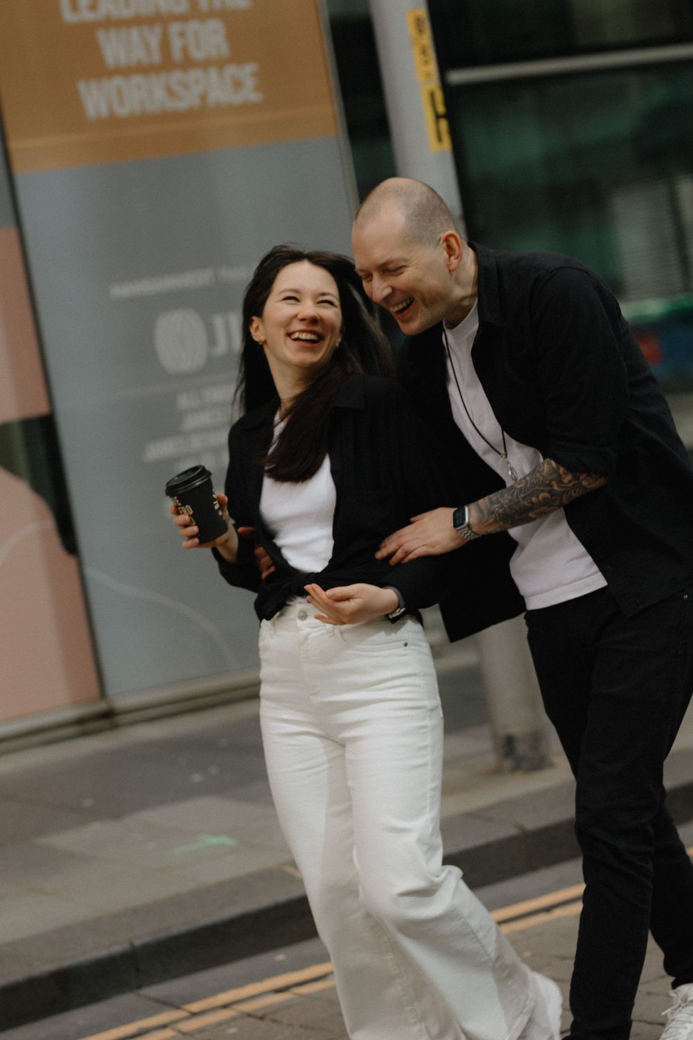 A couple shares joyful laughter and embraces outside an urban workspace building.