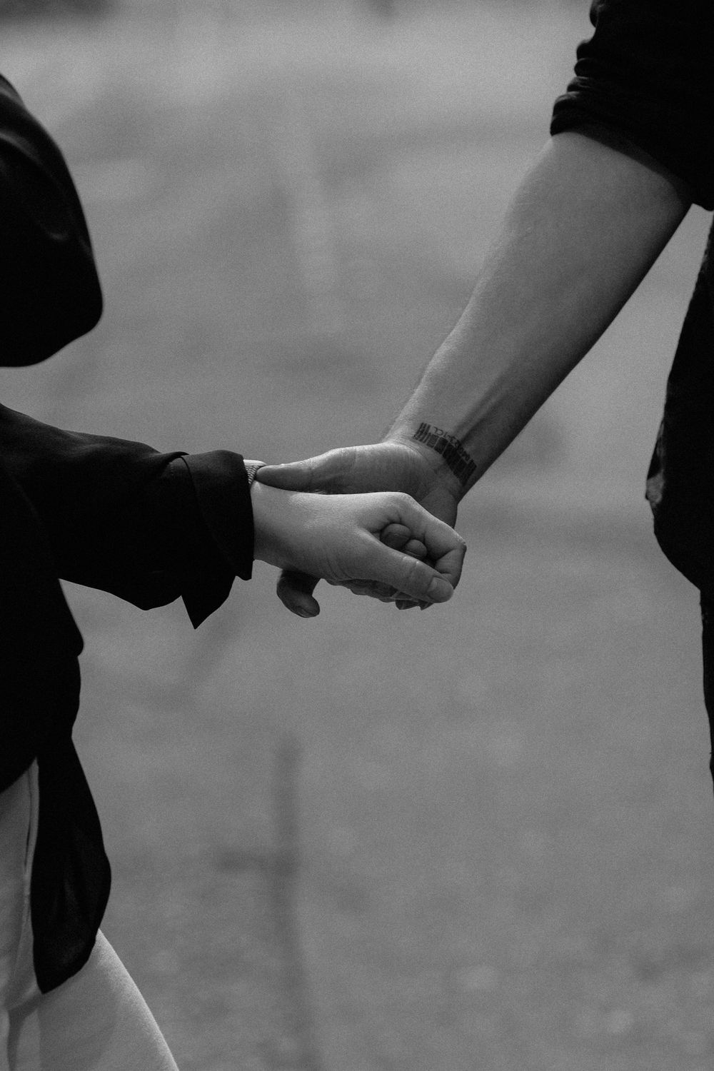 Black and white close-up of two people holding hands tenderly in an intimate moment.