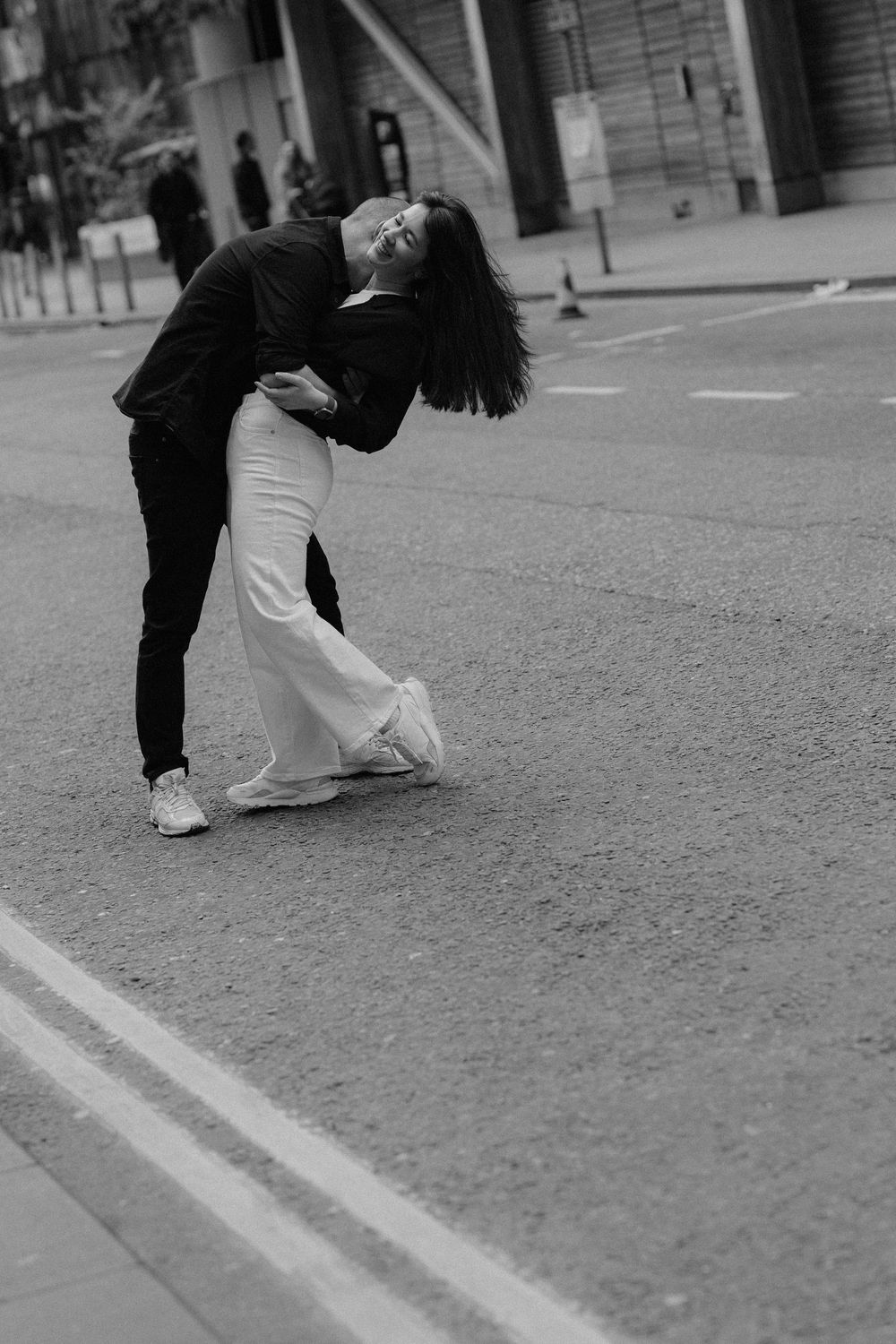 A couple embraces in a dramatic dance-like pose on an empty urban street in black and white photography.