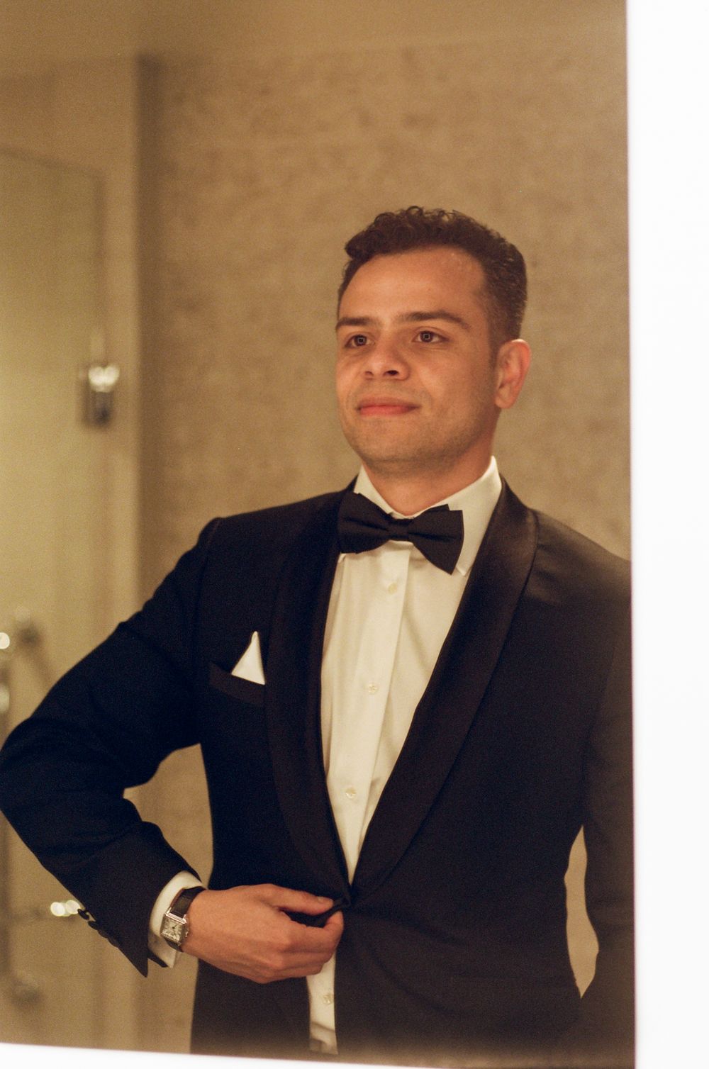 A person in formal black tuxedo and white shirt strikes four different poses against a beige wall.