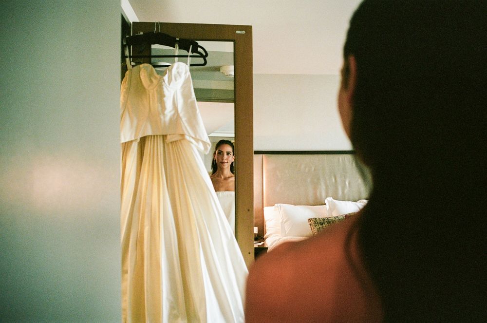 Wedding dress hangs in warm natural light streaming through window while getting ready for ceremony.