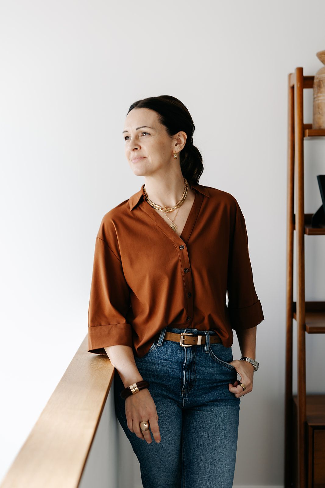 Person wearing brown polo shirt and jeans poses against white wall in minimalist portrait series.