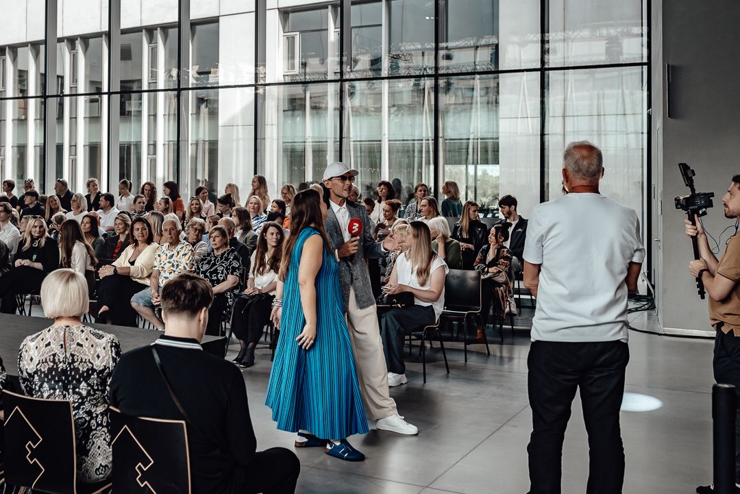 Wedding guests stand and applaud during a ceremony in a modern glass-walled venue with natural light.