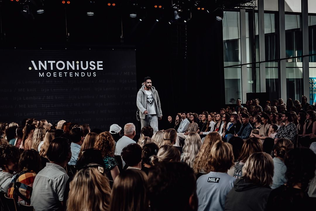 Fashion show audience members sit in rows watching models walk down a dark runway during a nighttime presentation.