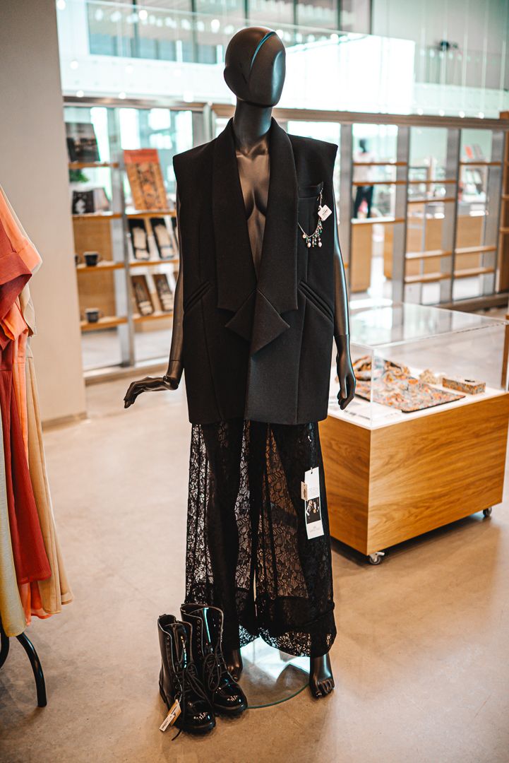 Black lace evening gown and blazer displayed on mannequins in an upscale retail boutique setting.