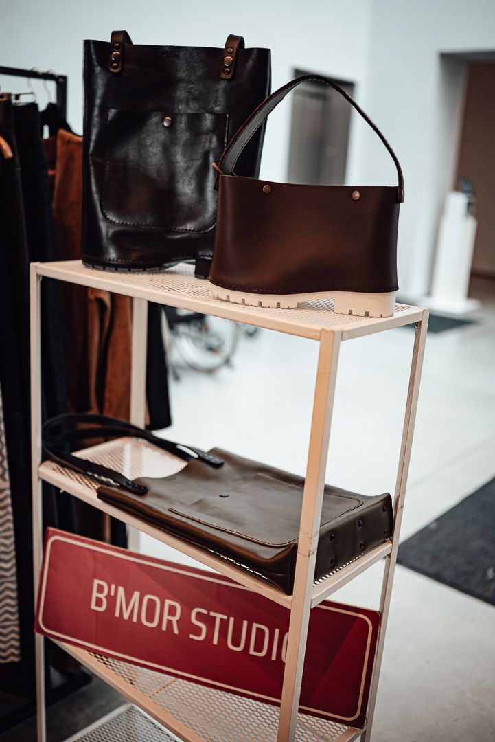 Black leather bags displayed on wooden shelving with red signage in a minimalist retail store interior.