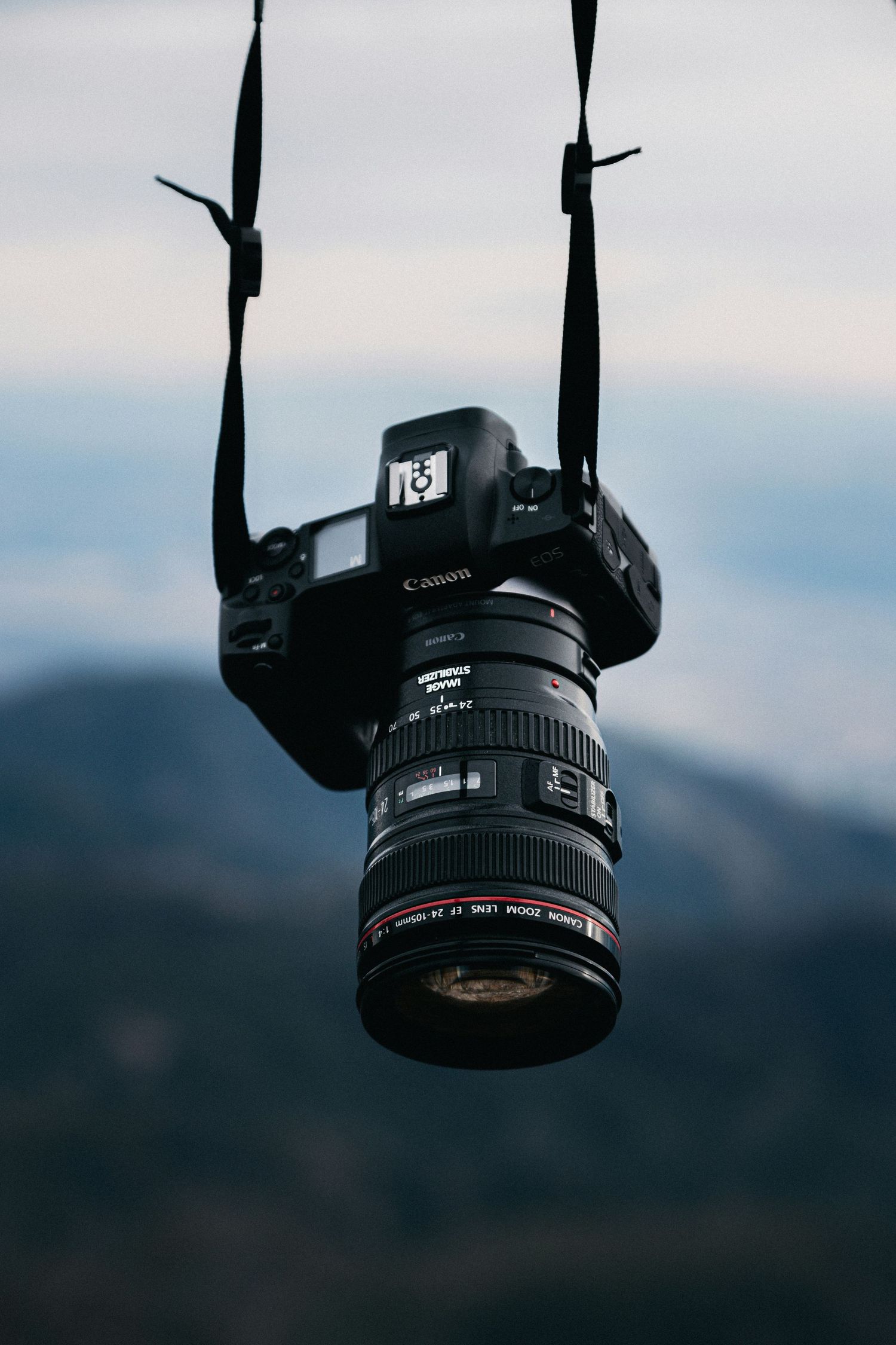 A Canon DSLR camera with lens shown in multiple silhouetted angles against a blurred blue sky background.