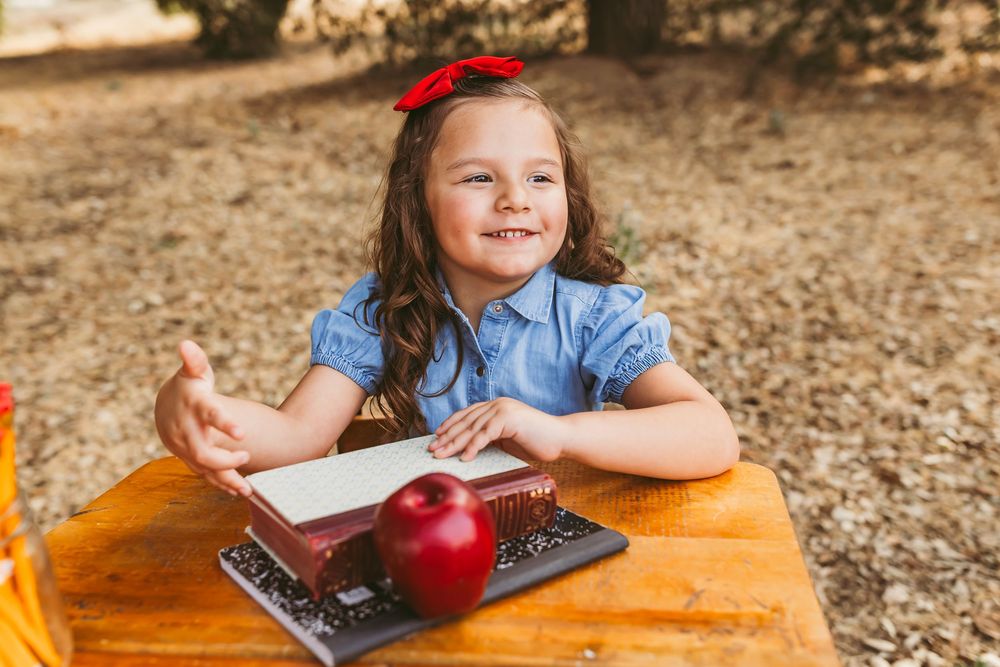 Student working at wooden table outdoors with a bright red apple and textbooks.