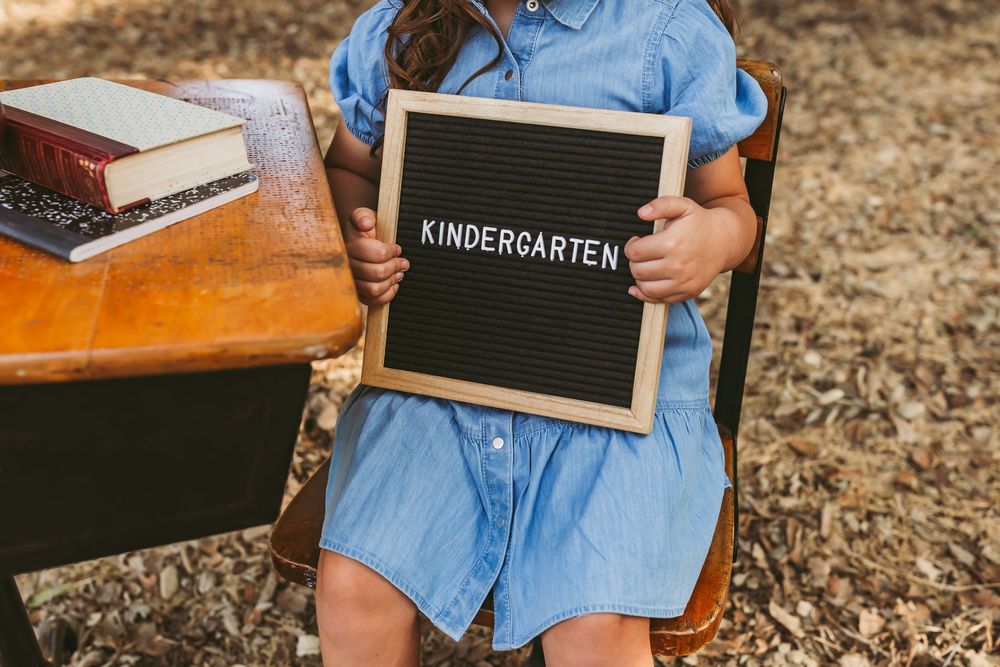 Small chalkboard sign reading 'Kindergarten' placed on a wooden surface near autumn leaves.