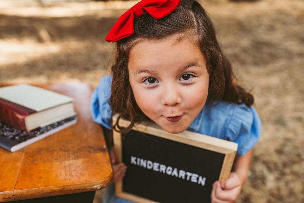 Kindergarten learning scene with chalkboard sign and bright red bow against natural background.