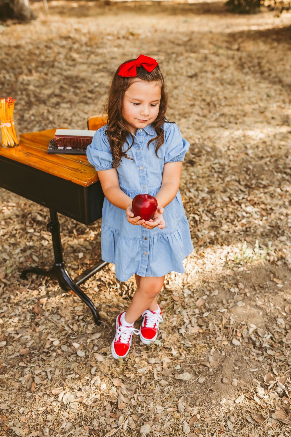 Blue dress clad student seated at rustic outdoor table with shiny red apple for snack.