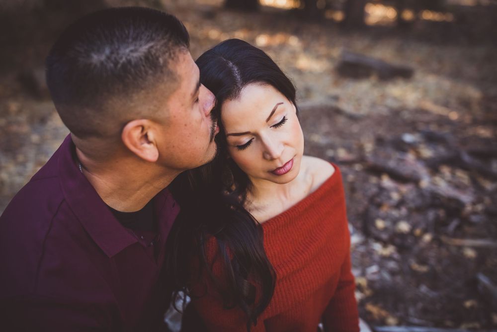 A couple in burgundy and red sweaters share an intimate moment outdoors during an autumn photoshoot.