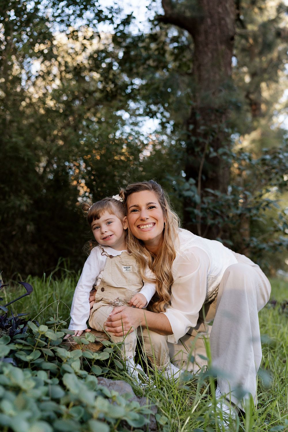 A candid outdoor portrait of two people sitting together on grass with trees in the background.
