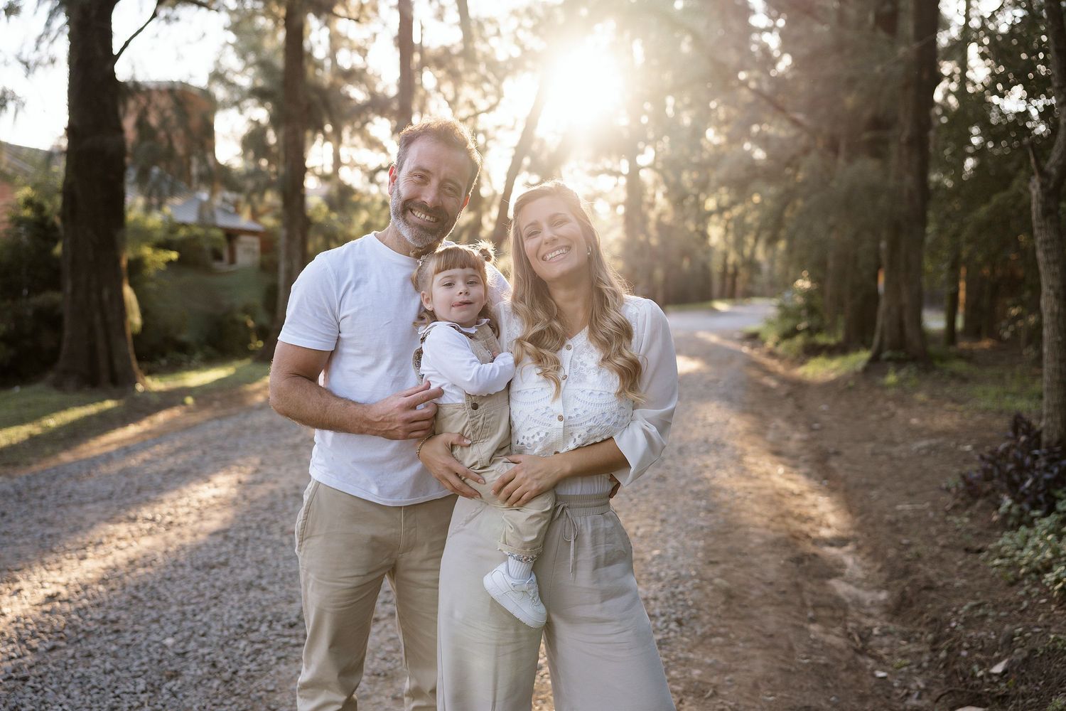 A family enjoys tender moments together on a sunlit gravel path at golden hour, creating a warmth-filled outdoor scene.