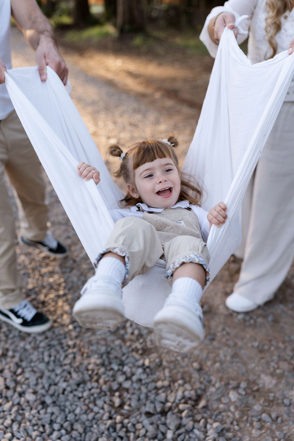 Children playing and spinning in flowing white dresses and outfits on gravel path during an outdoor photo session.