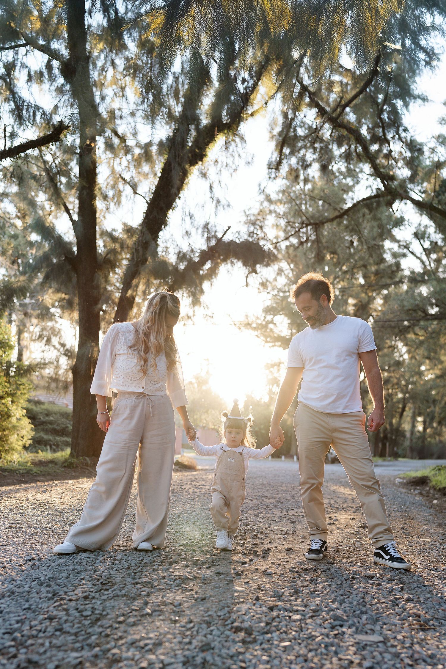 A group in white shirts and khaki pants walks together on a sunlit nature path among trees.