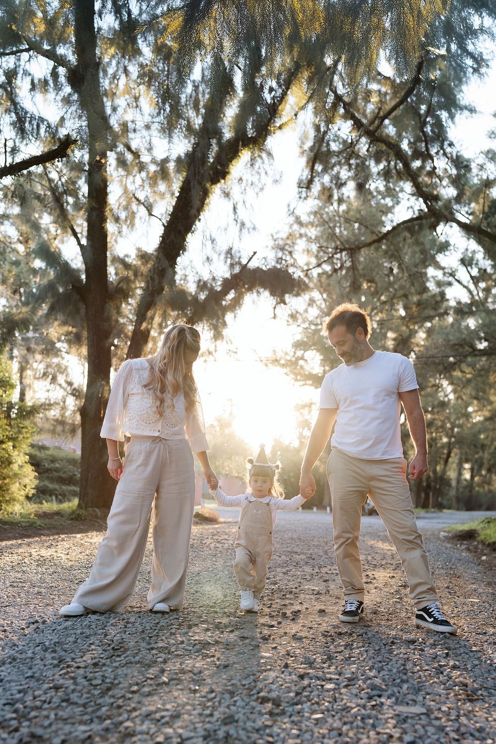 A group in white shirts and khaki pants walks together on a sunlit nature path among trees.