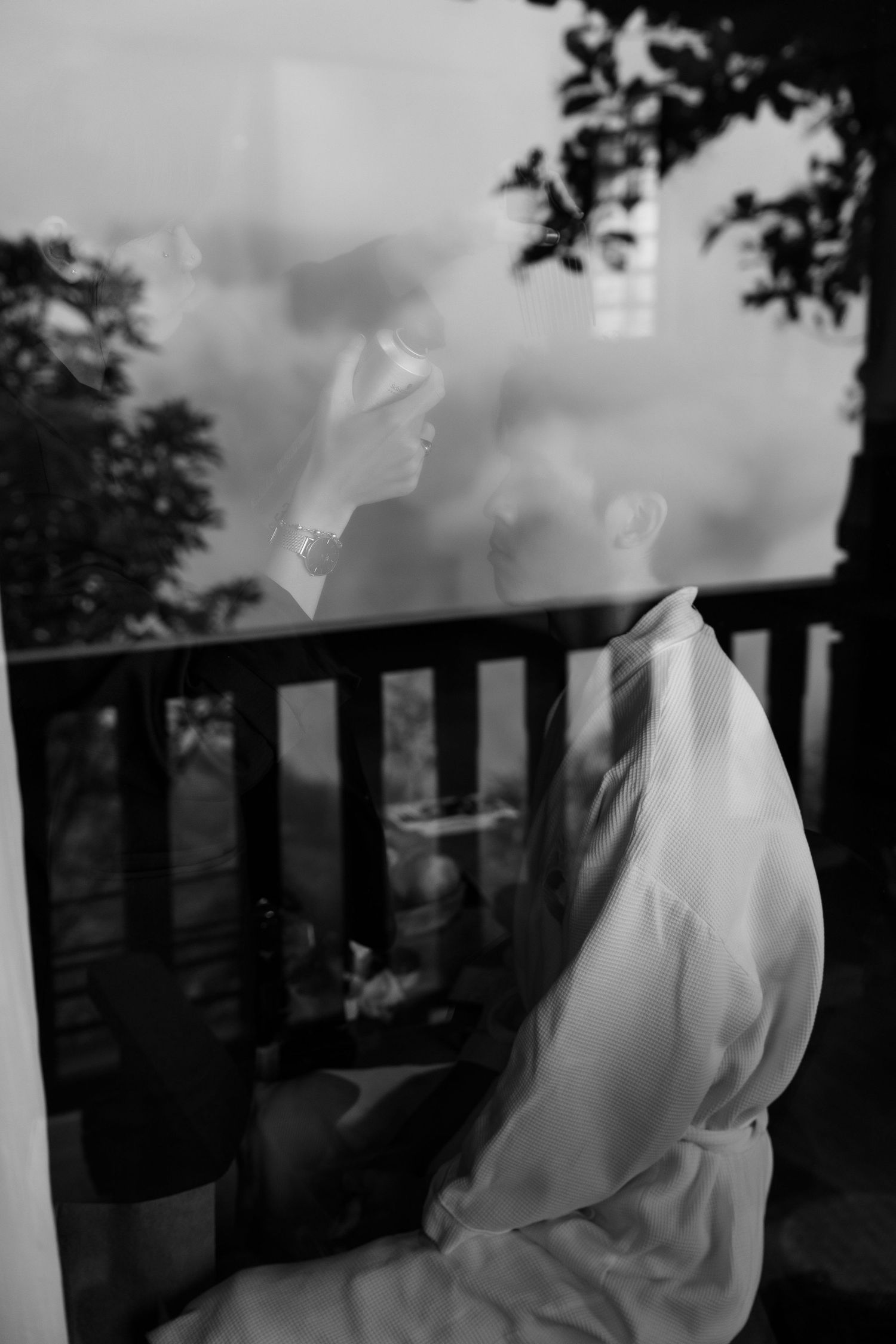 Black and white reflection of bride in white dress through rain-streaked window.