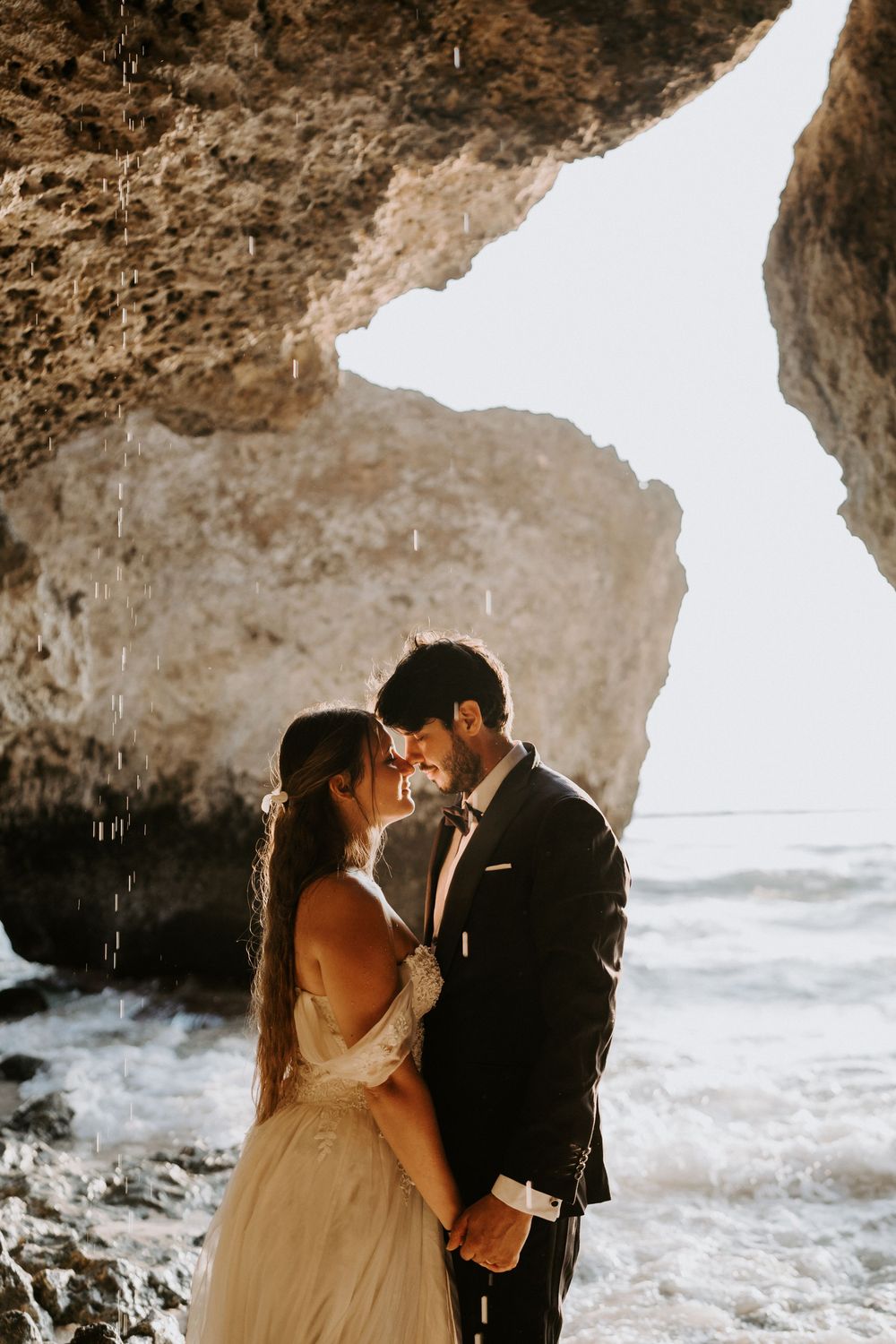 Intimate wedding moment captured beneath a rocky seaside cave formation.