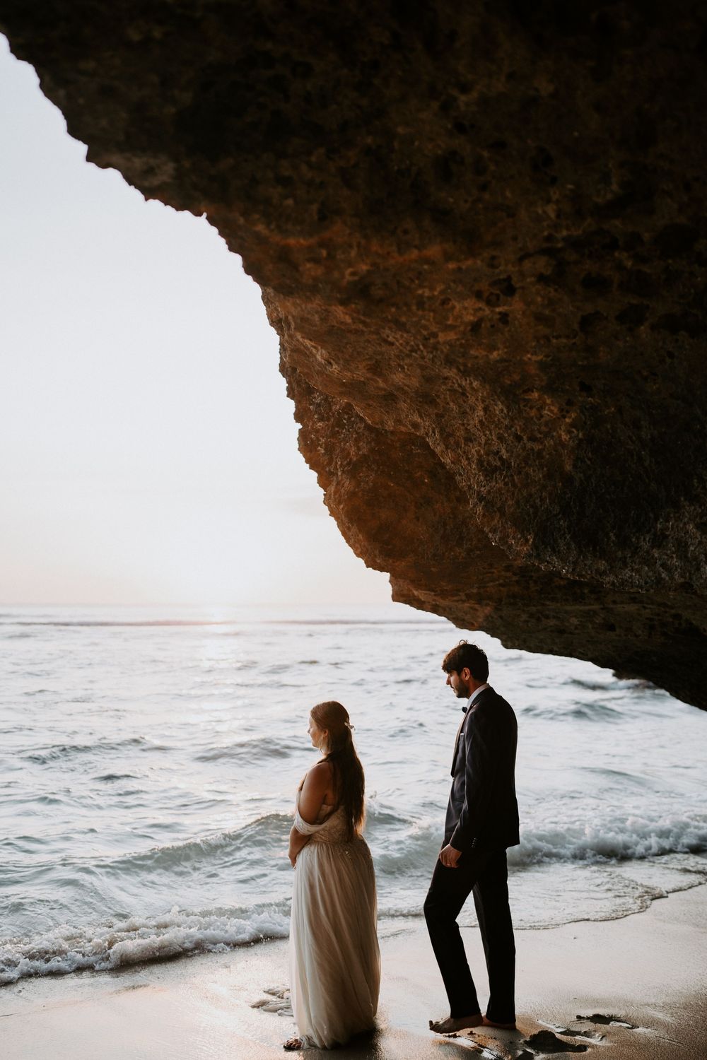 Wedding couple shares a special moment in a scenic beach cave overlooking the sea.