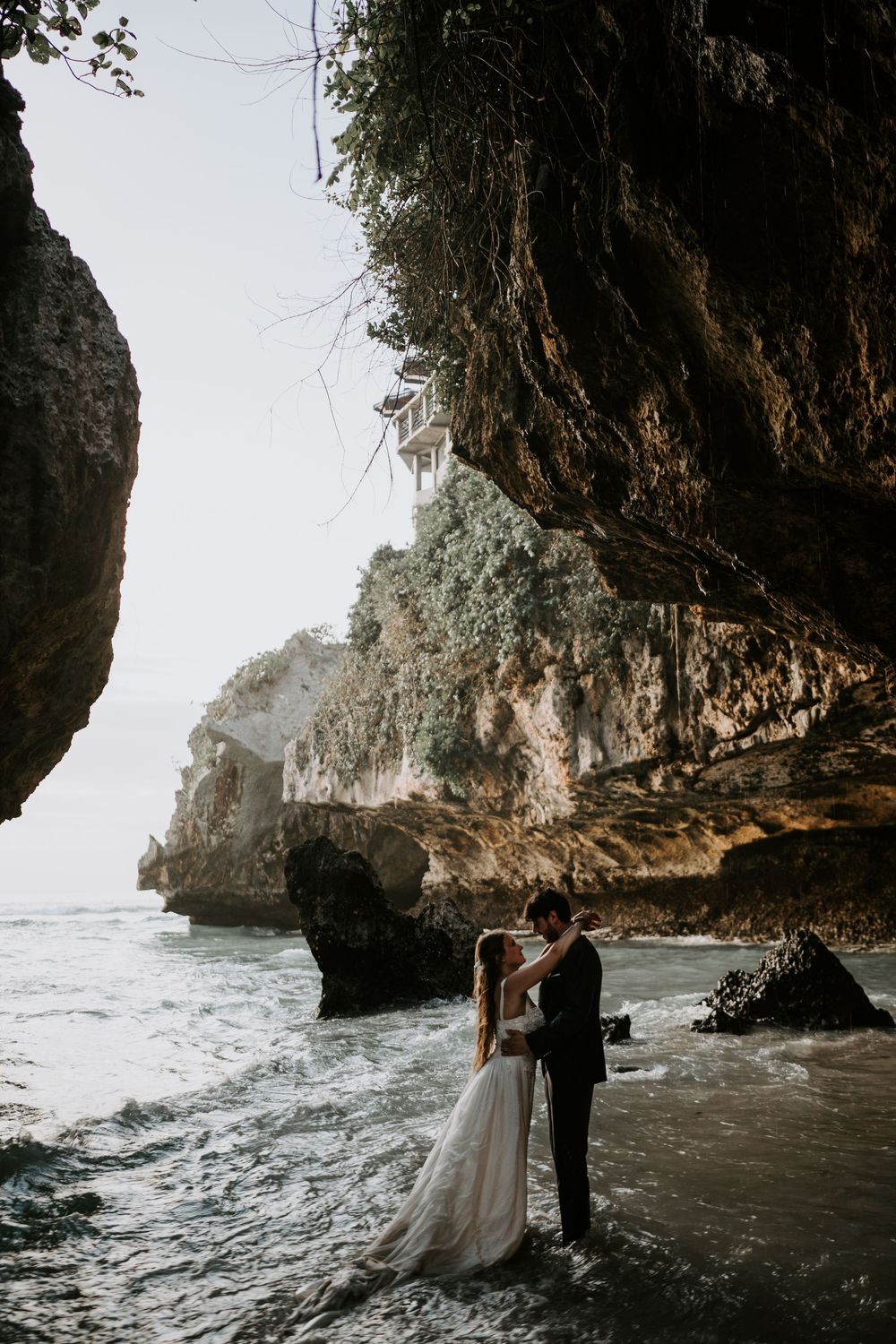 Dramatic wedding photography in a seaside cave with crashing waves in the background.