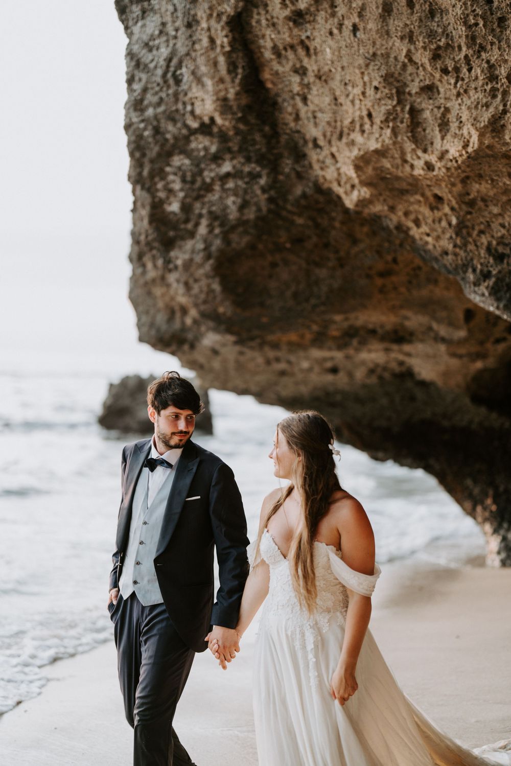 Romantic beach portraits under large limestone cliffs with crashing waves.