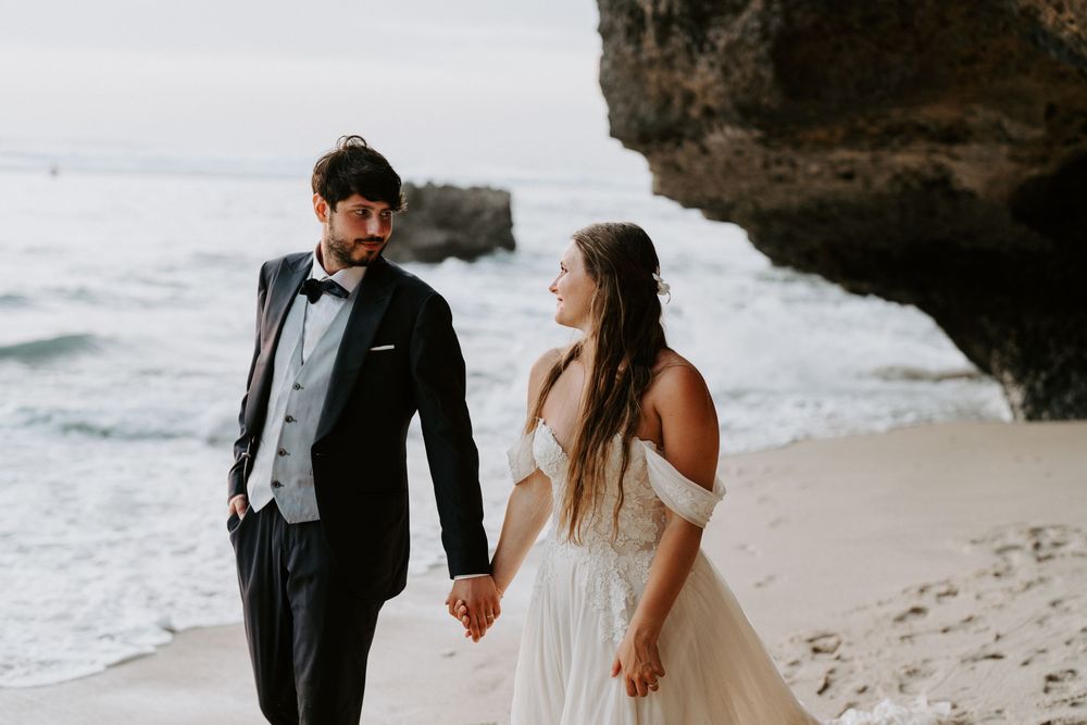 Couple holding hands near dramatic coastal rock formations on a beach.