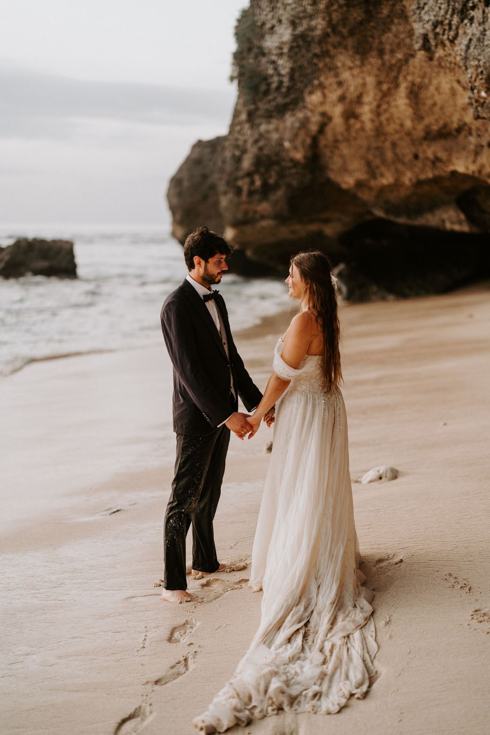 Elegant beach wedding photos with dramatic rock formations in background.
