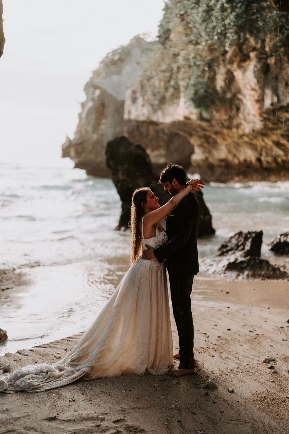 A romantic beach wedding photoshoot under dramatic coastal cliffs at sunset.