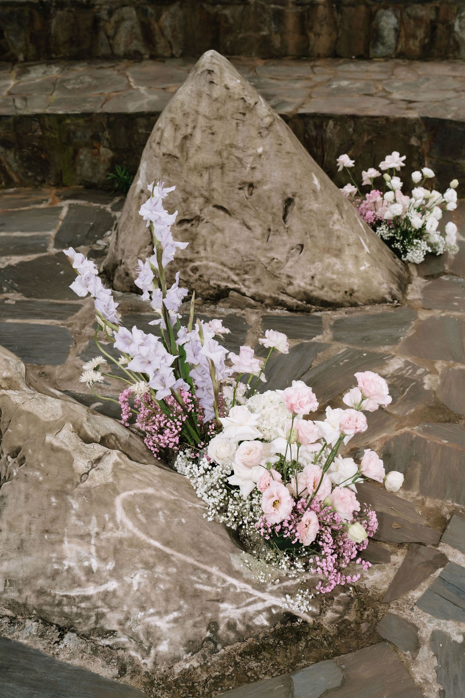Pink and white floral arrangement with gladiolus and roses placed on natural stone steps outdoors.