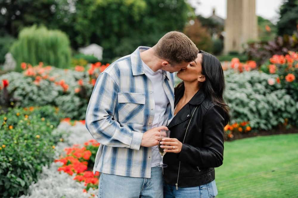 A couple laughs together in a garden setting surrounded by vibrant orange blooms and decorative landscaping.