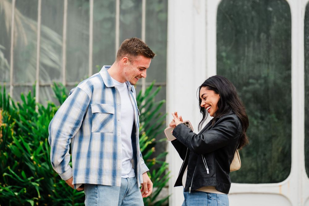 Two people walking and laughing together outside while wearing plaid and black jackets in a nature setting.