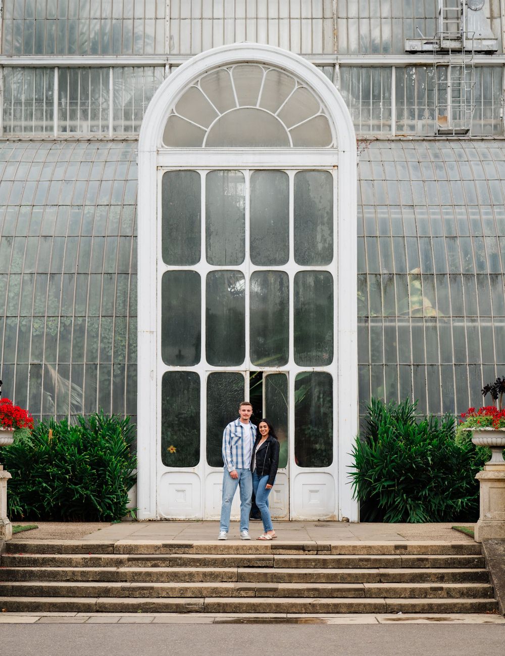 People stand outside a historic greenhouse or conservatory with arched windows and white architectural details.