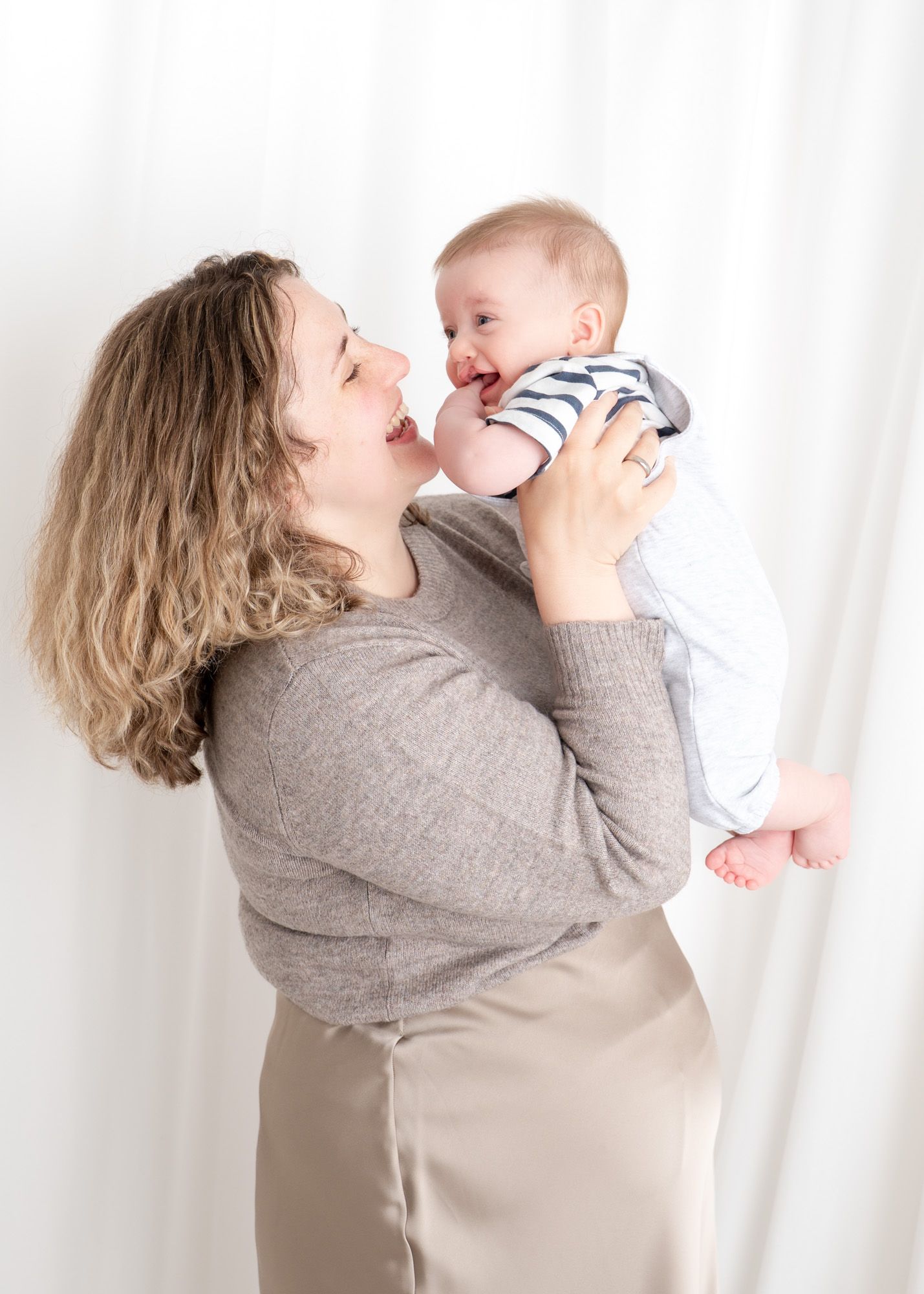 A joyful moment between parent and baby against white backdrop.