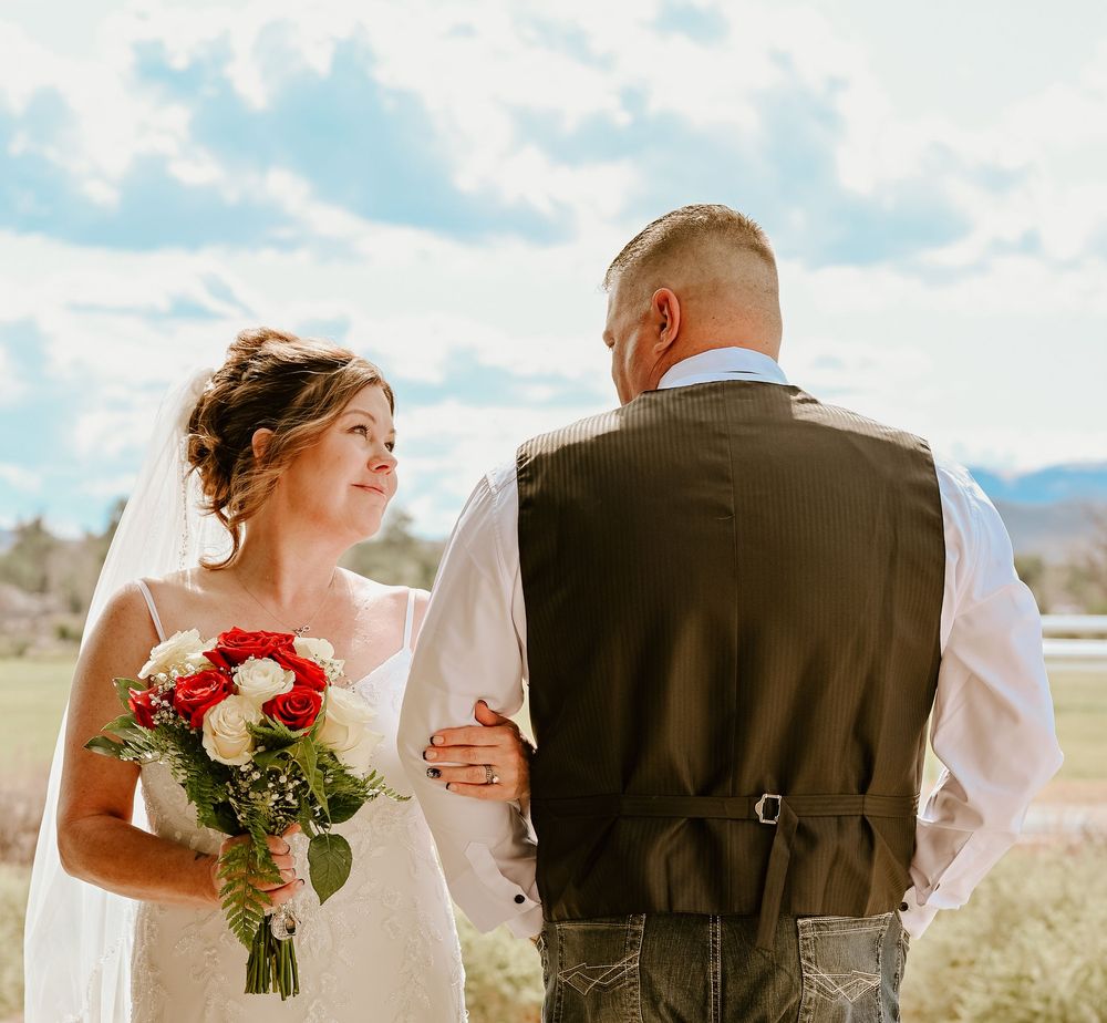 Newlyweds embrace during a romantic outdoor desert wedding ceremony with mountains and blue sky in the background.