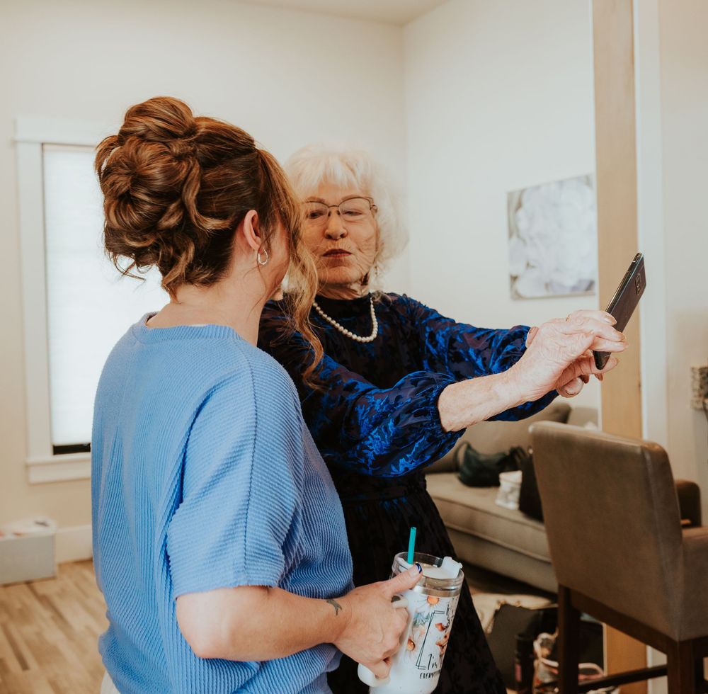 Healthcare worker in blue scrubs assists an elderly person in a navy blue dress during a home care visit.