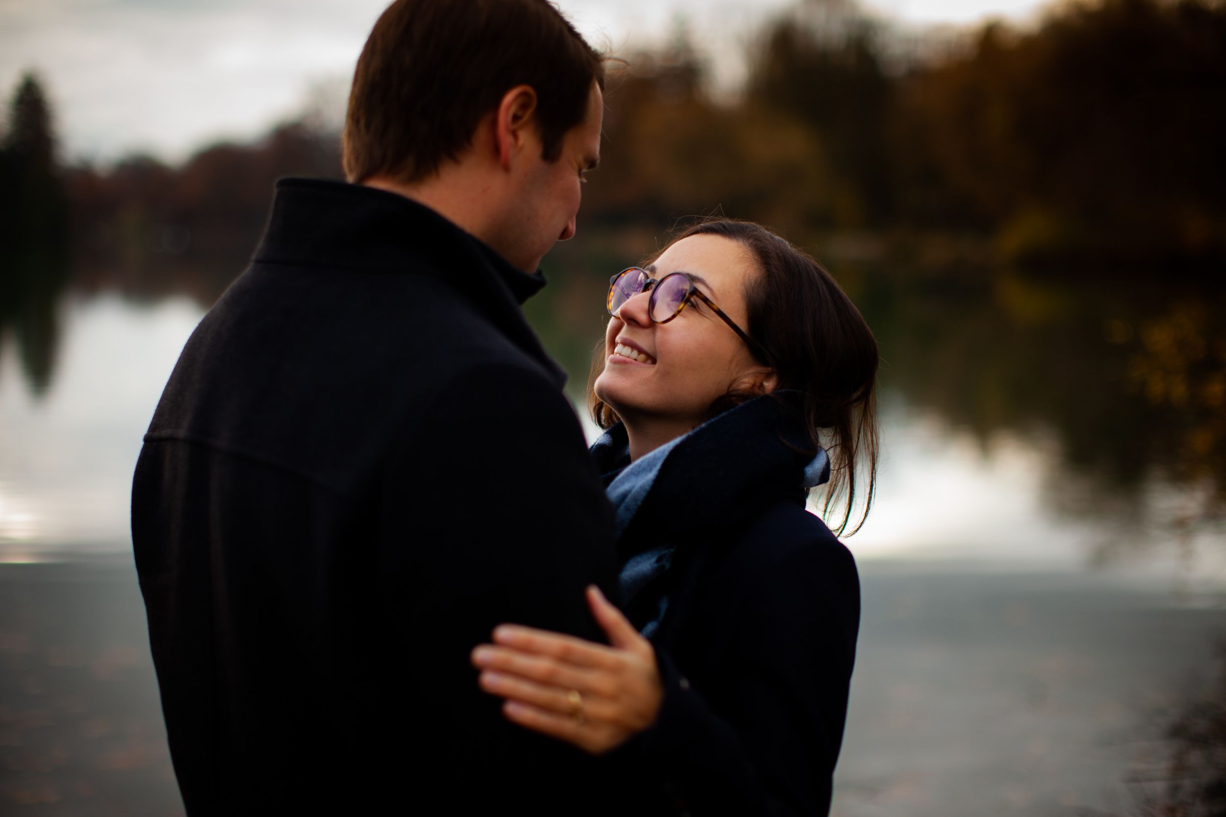 Happy couple embraces while laughing together by a lake at sunset creating a romantic outdoor moment.