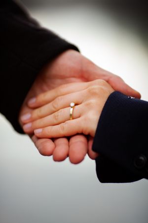 Close-up of two hands clasped together, with one hand wearing a gold wedding ring against a soft blurred background.