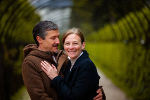 A couple shares an intimate moment on a path surrounded by lush green ferns and foliage.