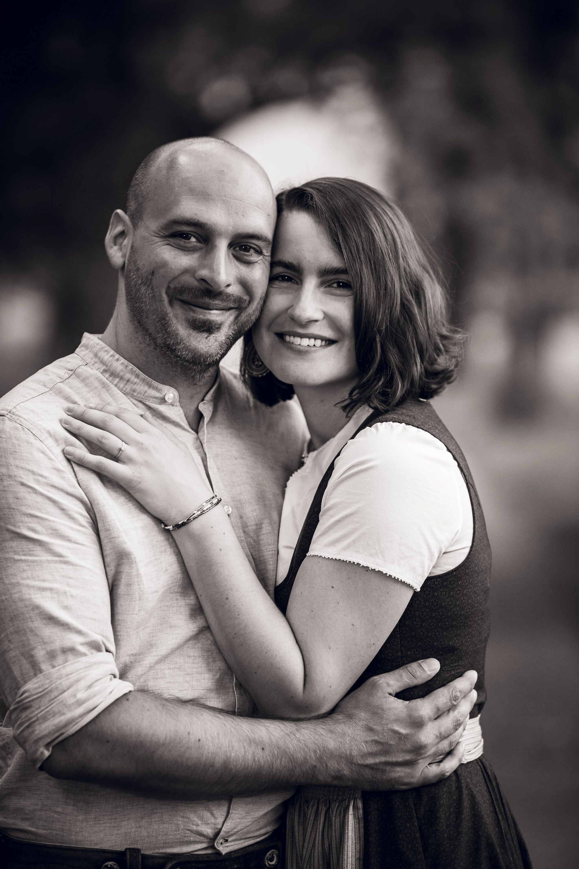 A romantic black and white portrait of a couple embracing and smiling together outdoors.
