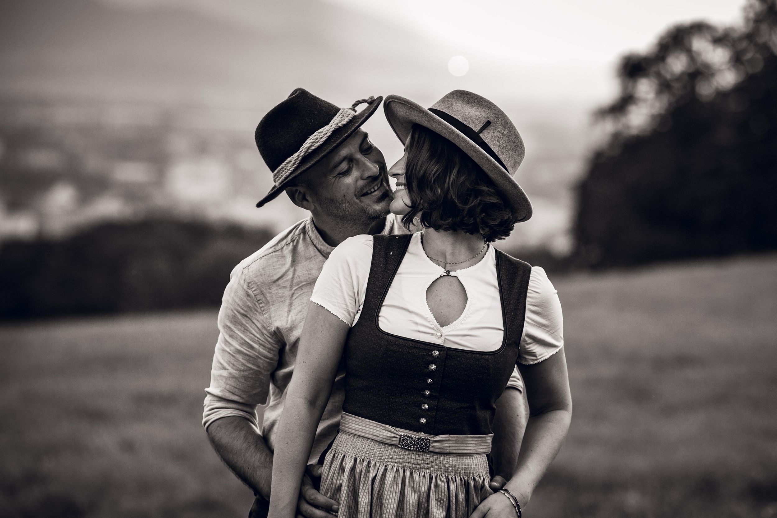 A romantic black and white photograph of a couple in vintage attire sharing an intimate moment outdoors.