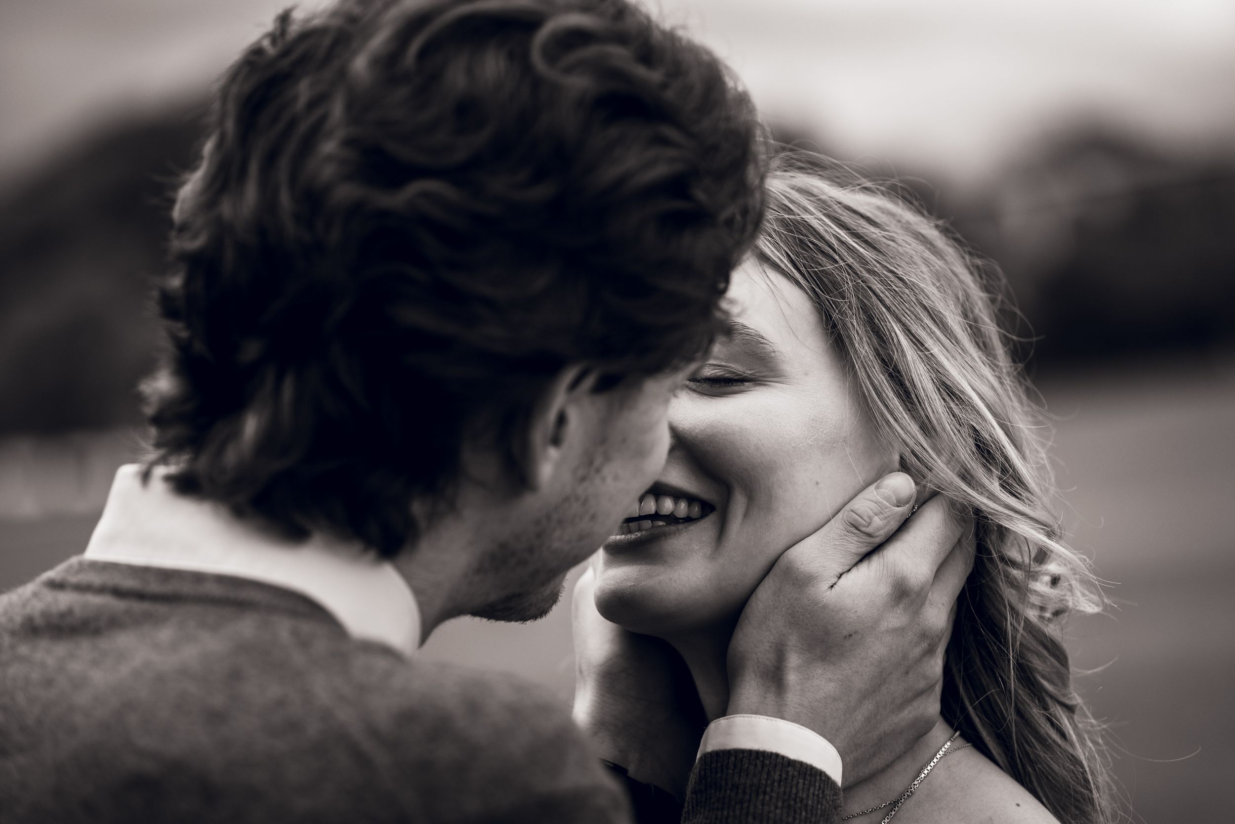 Black and white romantic couple photo, man tenderly cupping womans face as she smiles, outdoor engagement shoot.