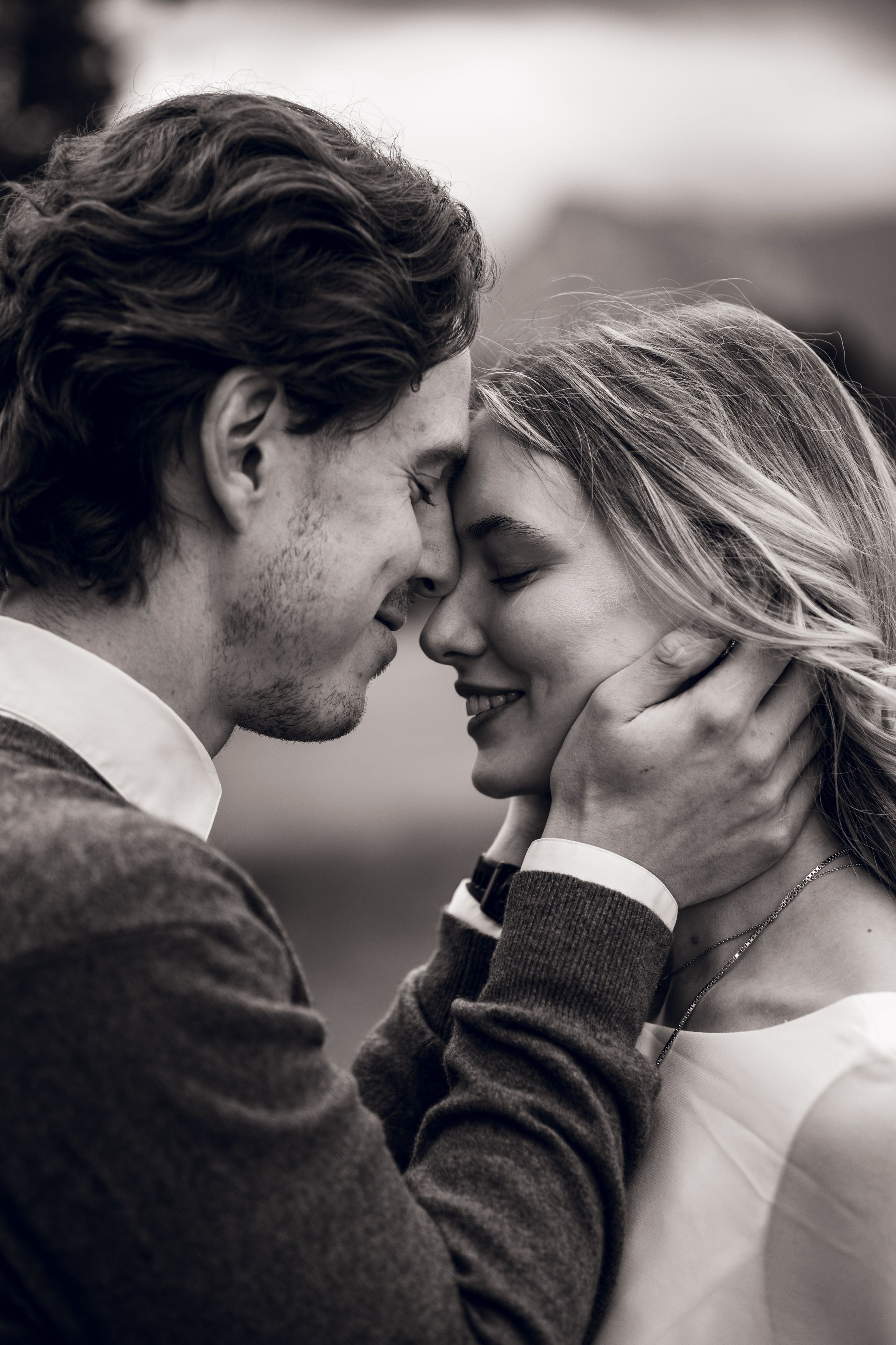 Black and white photo of a romantic couple sharing an intimate moment, man tenderly holding womans face as they lean close together.