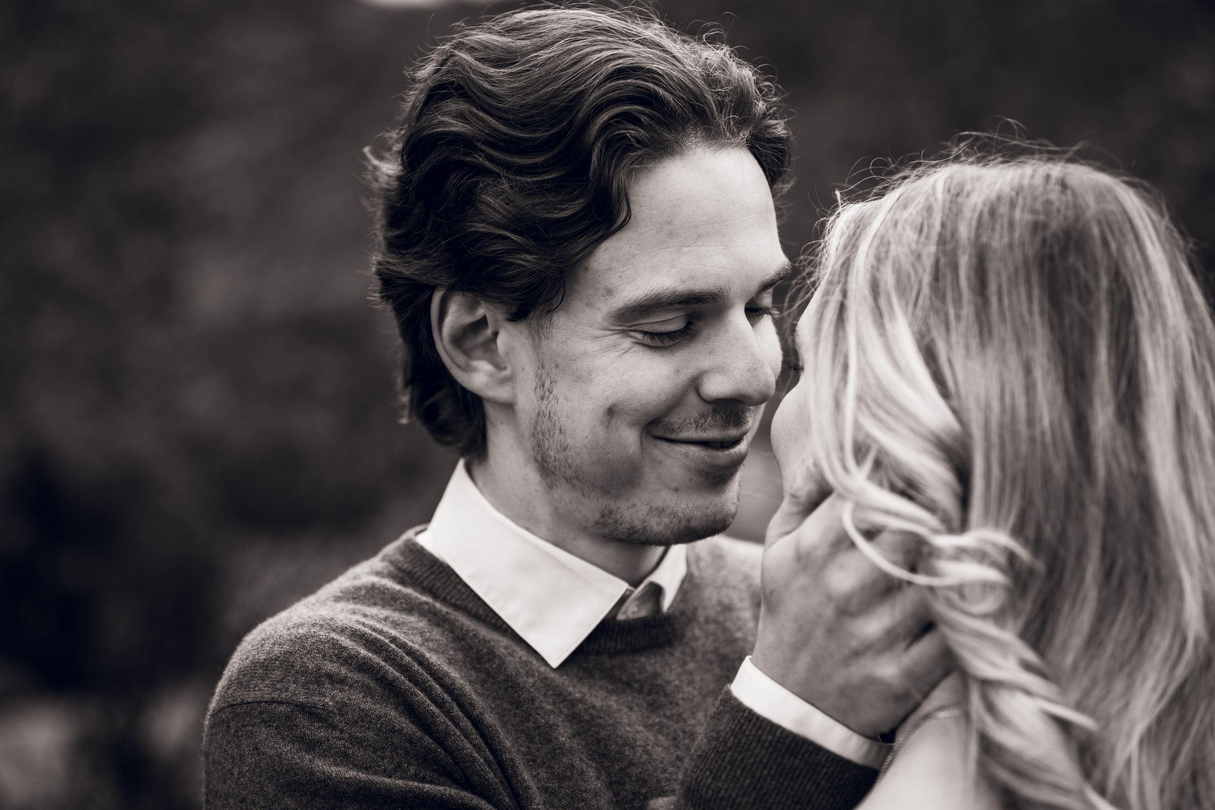 Black and white photo of a smiling man leaning in close to a blonde woman in a romantic outdoor setting.