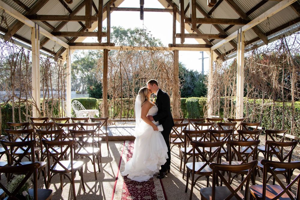 Empty rustic barn wedding ceremony venue with wooden cross beams and rows of chairs set up for guests.
