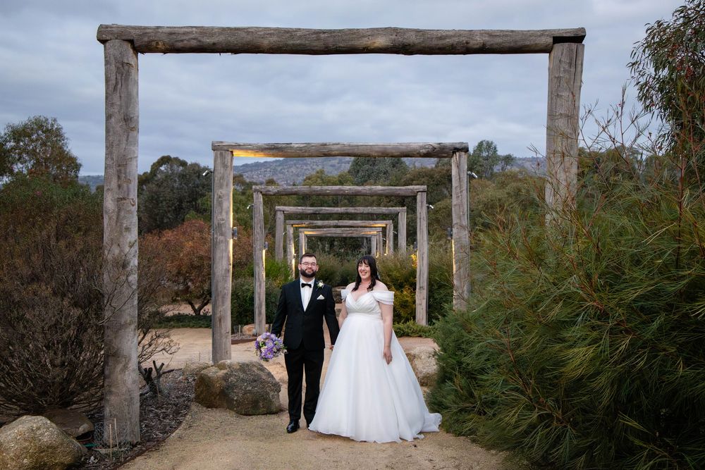 A picturesque wooden pergola creates a rustic archway path leading through a garden landscape.