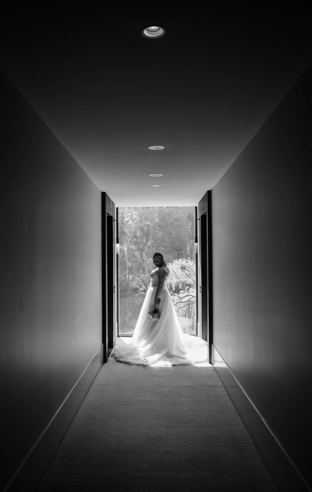 Dramatic black and white silhouette in a hallway shows a figure in flowing gown standing in bright doorway.