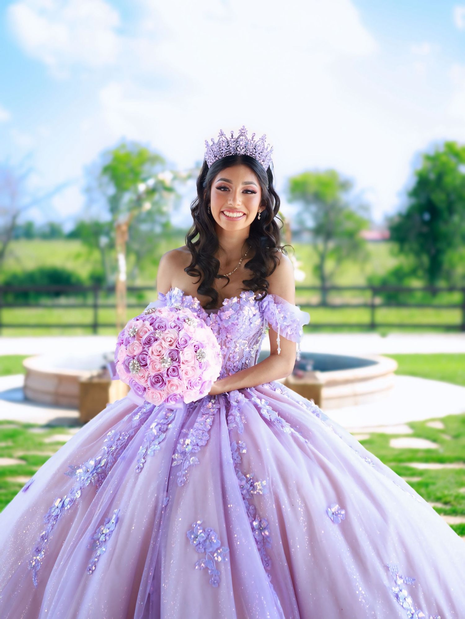A lavender quinceañera dress with floral appliques and a full tulle skirt photographed outdoors in a garden setting.